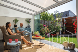 Witte aluminium overkapping aan huis met glazen schuifwanden in de tuin